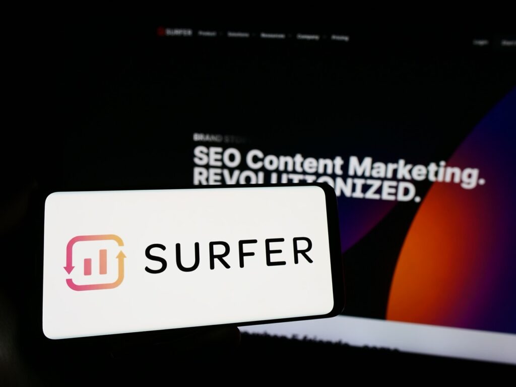 Person holding smartphone with logo of Polish AI company Surfer sp. z o.o. (SurferSEO) in front of website. Focus on phone display. Unmodified photo.
